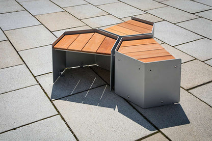 Moderner Outdoor-Sitz mit dreieckigem Design, Holzoberfläche und Metallrahmen auf gepflastertem Boden.