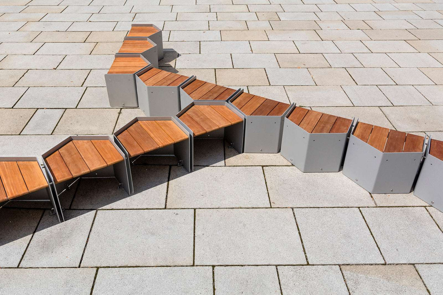 Modulare Holzbänke in hexagonaler Form auf gepflastertem Boden arrangiert.